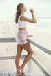 Young woman on a balcony, drinking water from a bottle, seaside