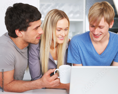 Photo: Happy friends using a laptop in the kitchen Happy friends using a laptop in the kitchen