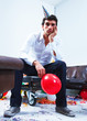 Unhappy boy wearing a party hat and sitting in a messy living ro