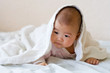 Baby on her stomach peeking from under a blanket