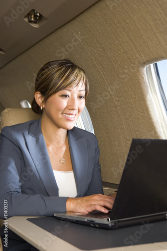 Photo: Businesswoman using laptop computer on aeroplane, smiling, close-up Businesswoman using laptop computer on aeroplane, smiling, close-up