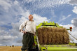 Portrait of farmer standing near machinery with straw bale