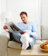 Man relaxing on couch at home reading newspaper