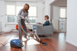 Woman vacuum cleaning man watching tv