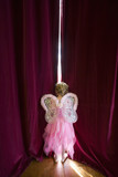 Photo: Ballerina girl (4-6) with fairy wings peeking out gap in stage curtains, rear view Ballerina girl (4-6) with fairy wings peeking out gap in stage curtains, rear view