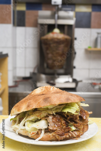 Photo: a döner kebab with meat on spit in background a döner kebab with meat on spit in background