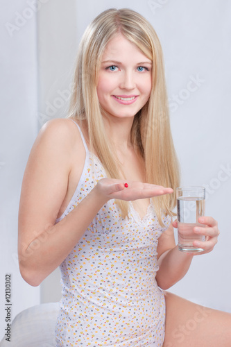 Photo: Woman in bedroom holding red capsule in hand and glass of water Woman in bedroom holding red capsule in hand and glass of water