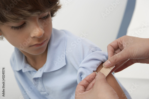 Photo: Nurse placing bandage on boy's arm,close up Nurse placing bandage on boy's arm,close up