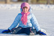 Girl on skates sitting on the ice.