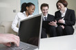 Hand working on laptop with business people in background.