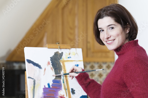 Photo: Smiling young woman painting on a drawing paper. Smiling young woman painting on a drawing paper.