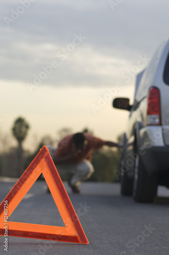 Foto: Warning triangle in front of broken down car, man in background Warning triangle in front of broken down car, man in background
