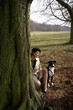 Frau und Jagdhund versteckt hinter Baum