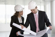 Two architects wearing hard hats looking at plans