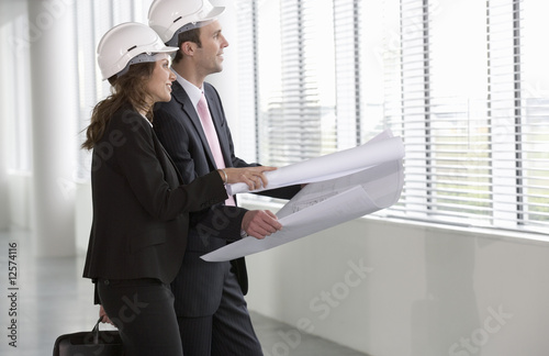 Photo: Two architects wearing hard hats looking at plans Two architects wearing hard hats looking at plans