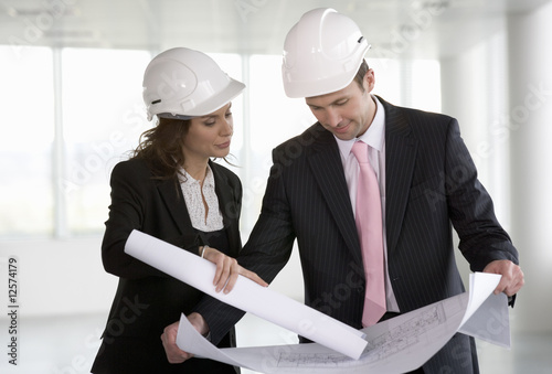 Photo: Two architects wearing hard hats looking at plans Two architects wearing hard hats looking at plans