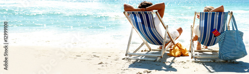 Photo: Couple on a deck chair relaxing on the beach, rear view Couple on a deck chair relaxing on the beach, rear view