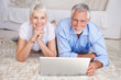 Foto: Happy senior couple lying down with a laptop Happy senior couple lying down with a laptop