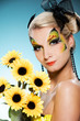 Young beauty with butterfly face-art and bouquet of sunflowers