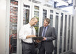 Two mature man checking computers in server room