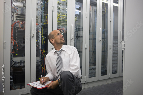 Photo: Mature man checking computers in server room Mature man checking computers in server room