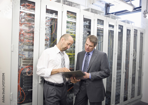Photo: Two mature man checking computers in server room Two mature man checking computers in server room
