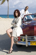 Young multi-ethnic couple with car on beach, young woman leaning on car in foreground, Havana, Cuba