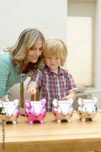 Photo: Mother and son putting coin in piggy bank, smiling, Den Haag, Netherlands Mother and son putting coin in piggy bank, smiling, Den Haag, Netherlands