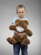 Young boy hugging a teddy bear wearing a mask, studio shot