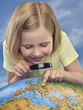 Young girl looking through a magnifying glass at a globe, studio shot