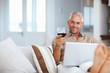 Mature man using a laptop while celebrating with wine