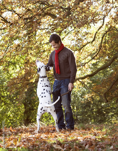 Photo: A young man playing with his dog amongst the autumn leaves A young man playing with his dog amongst the autumn leaves