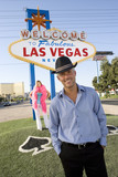 Photo: Portrait of mid-adult man in front of Welcome to Las Vegas sign, mid-adult woman behind. Portrait of mid-adult man in front of Welcome to Las Vegas sign, mid-adult woman behind.