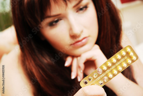Photo: Young woman looking at her contraceptive pills Young woman looking at her contraceptive pills