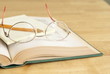 Eyeglasses with pencil and yellow notepad on open book