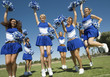 Group of Cheerleaders rising pom-poms, jumping on football field