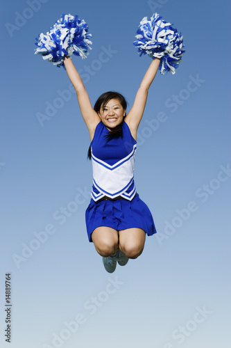 Photo: Smiling Cheerleader jumping in mid-air, portrait, low angle view Smiling Cheerleader jumping in mid-air, portrait, low angle view