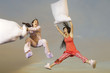 Two women having pillow fight mid-air outdoors