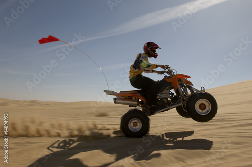Photo: Quad bike rider doing wheelie in desert, side view Quad bike rider doing wheelie in desert, side view