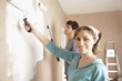 Couple using paint rollers on wall of living room
