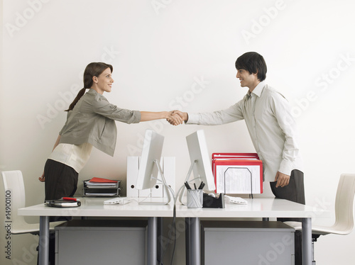 Photo: Man and Woman Shaking Hands over Desks, side view Man and Woman Shaking Hands over Desks, side view