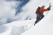 Mountain climber going up snowy slope with axes