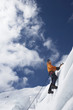 Mountain climber going up snowy slope with axes