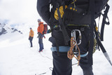 Photo: Hiker's back with backpack and safety rope in snowy mountains with two friends ahead, back view Hiker's back with backpack and safety rope in snowy mountains with two friends ahead, back view