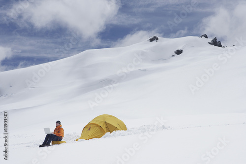 Photo: Hiker using laptop outside of tent on snowy mountain peak Hiker using laptop outside of tent on snowy mountain peak