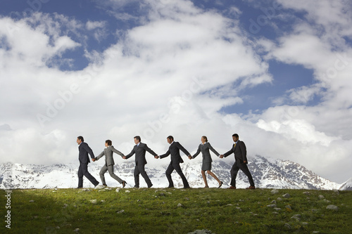 Photo: Business People Holding Hands and Walking through mountains, side view Business People Holding Hands and Walking through mountains, side view