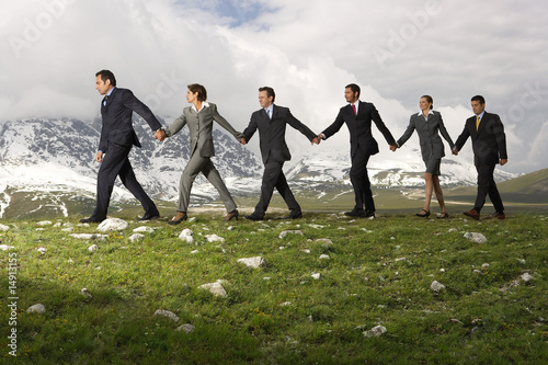Photo: Business People Holding Hands and Walking through mountains, side view Business People Holding Hands and Walking through mountains, side view
