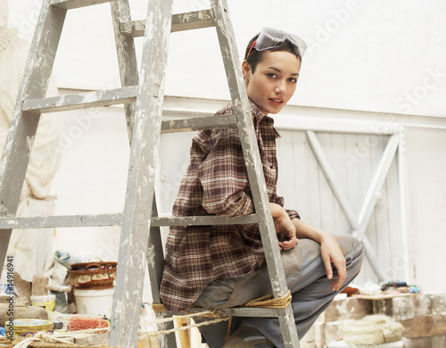Photo: Female interior decorator sitting on ladder in work site, portrait Female interior decorator sitting on ladder in work site, portrait