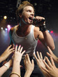 Low angle view of male rock star singing on stage with adoring fans reaching their hands up towards him