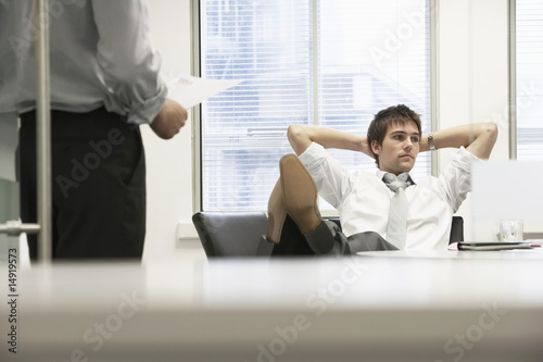 Photo: Disinterested businessman reclining on chair and ignoring boss in office Disinterested businessman reclining on chair and ignoring boss in office